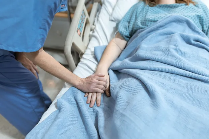 A nurse holding a patient’s hand beside a hospital bed