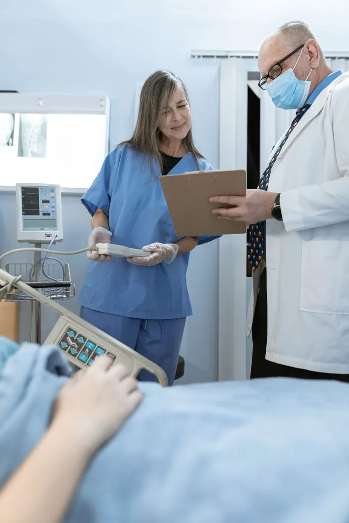 A nurse and doctor reviewing information together beside a hospital bed