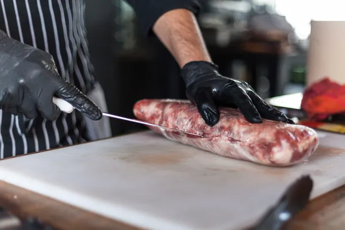 Gloved hands slicing a cut of meat on a preparation board