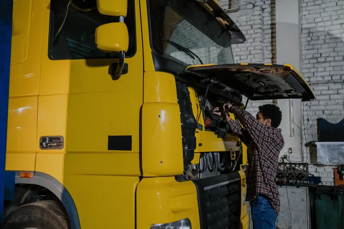 A mechanic working beneath the open engine cover of a truck